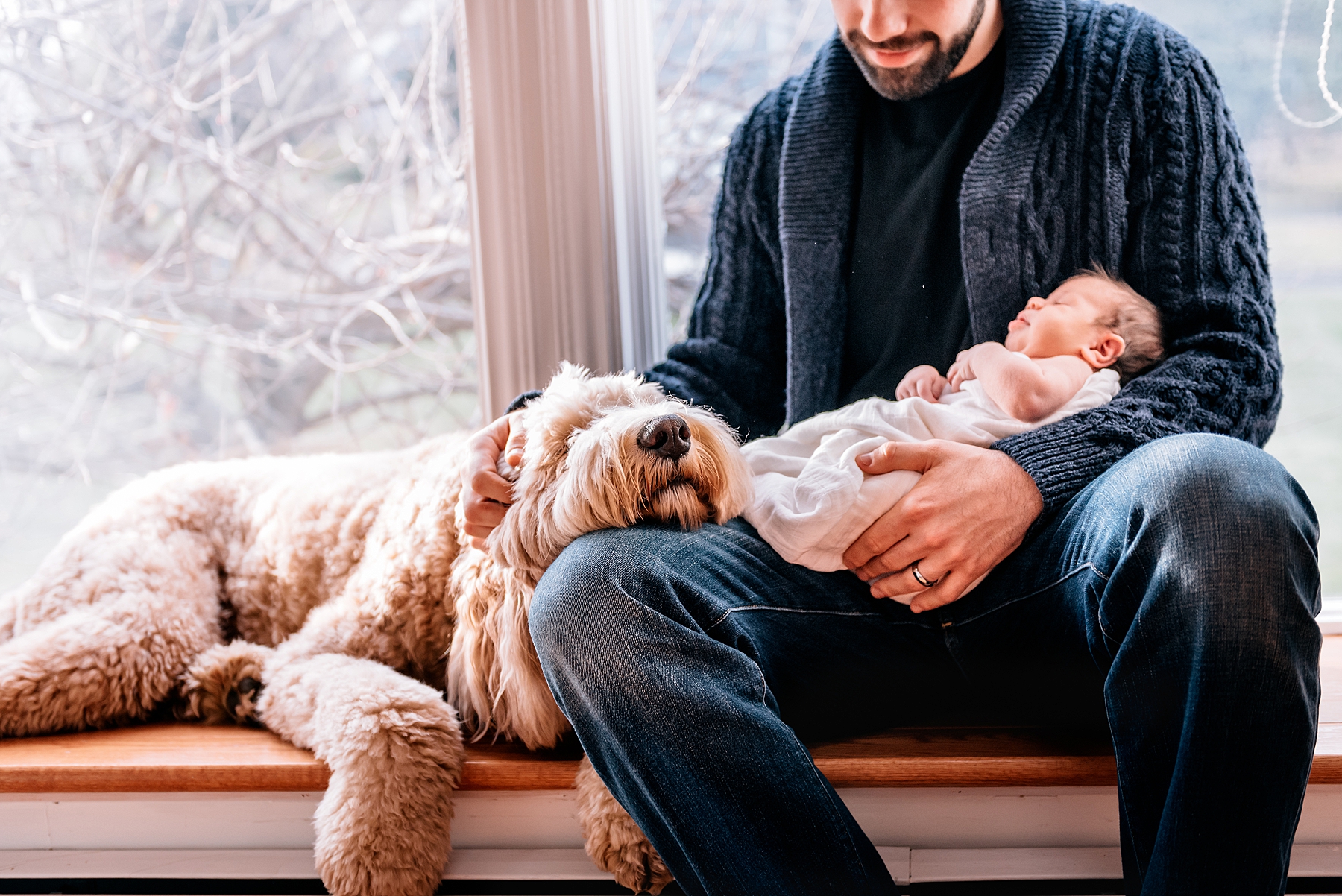 Dad holding his newborn baby and sitting next to his dog.