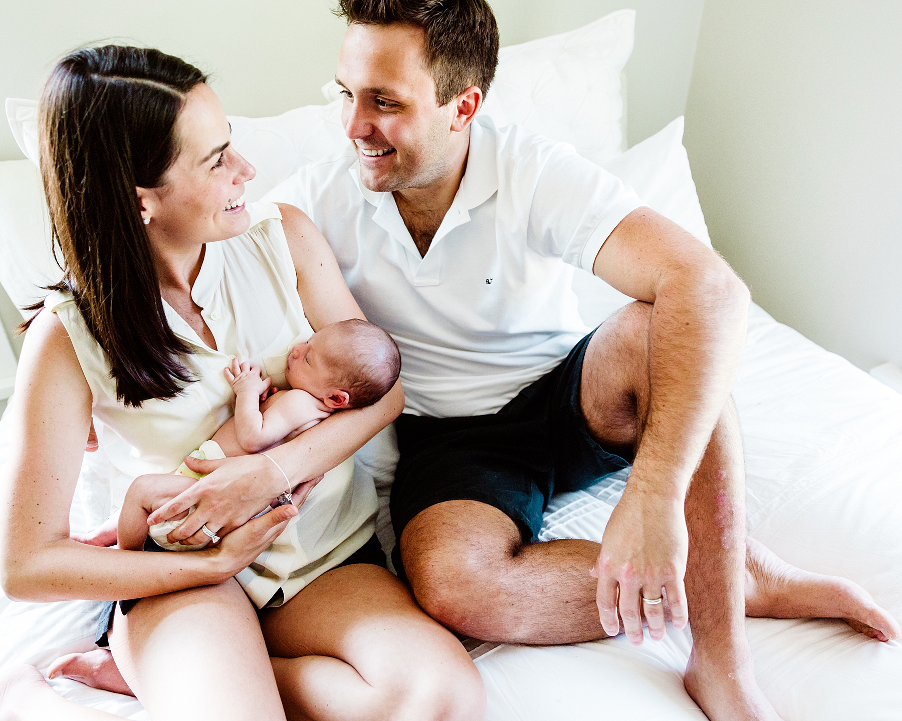 Mother and father hold newborn son while sitting on bed in home natural newborn photoshoot