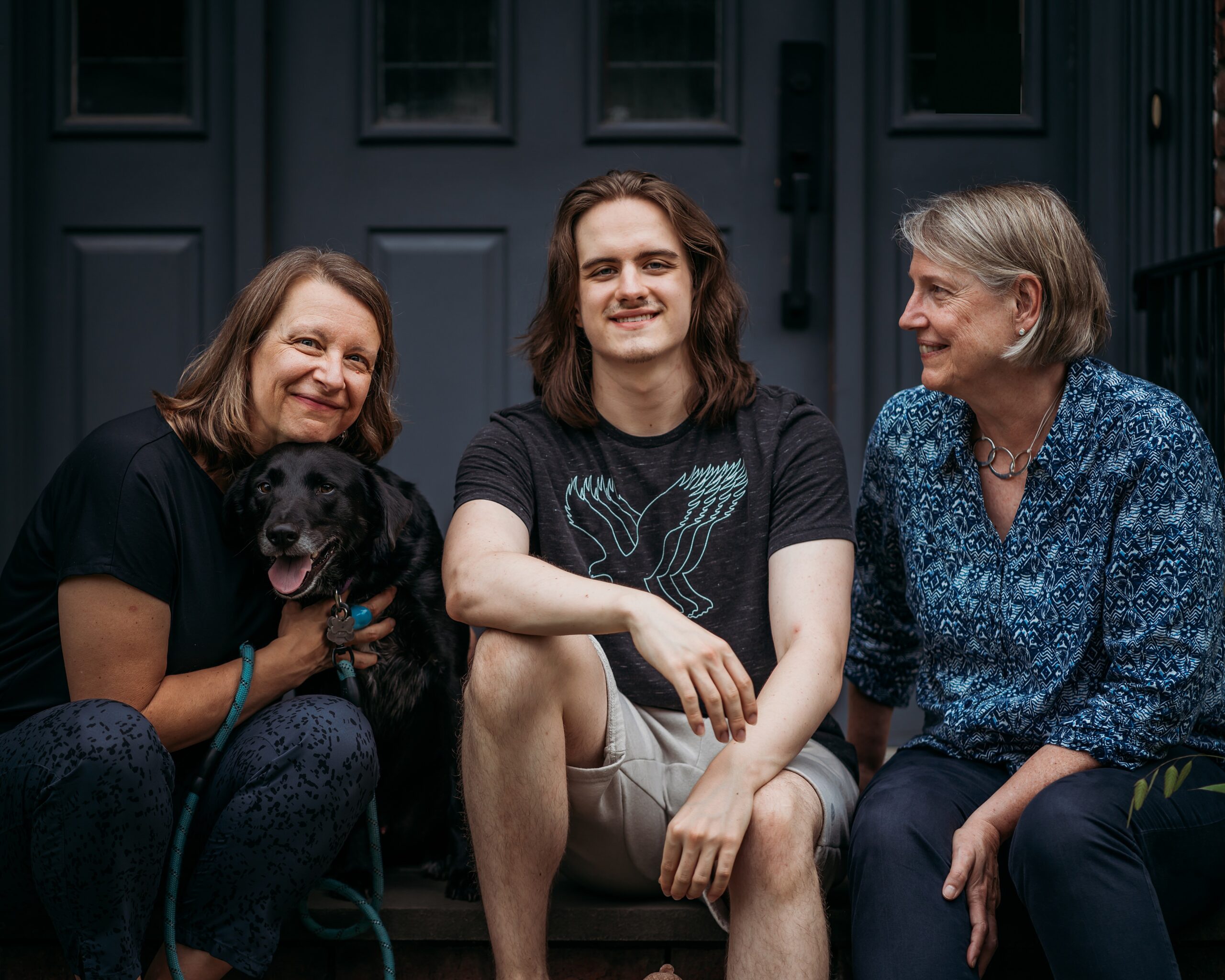 Two mothers and their son, sitting with their black dog.