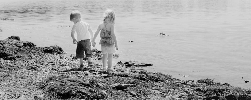 Black and white photo of two young children walking along the water's edge at the Marshlands Conservancy at the Long Island Sound.