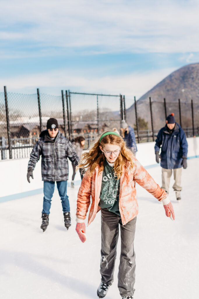 Family ice skating at Bear Mountain with mountains visible in the background.